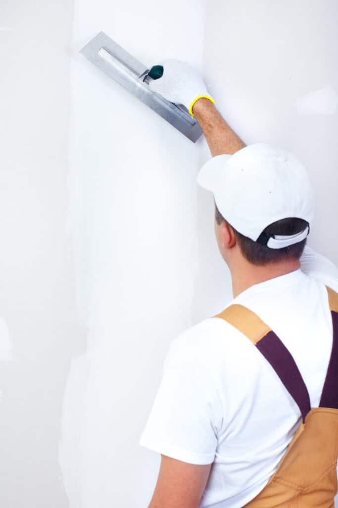 Plaquiste appliquant enduit mural avec taloche blanche Ouvrier appliquant de l'enduit sur un mur blanc avec une taloche, portant une casquette blanche.