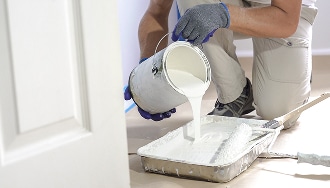 Peinture blanche : préparer l'application murale au rouleau Peintre en bâtiment versant de la peinture blanche d'un bidon dans un bac à peinture, prêt à appliquer avec un rouleau.